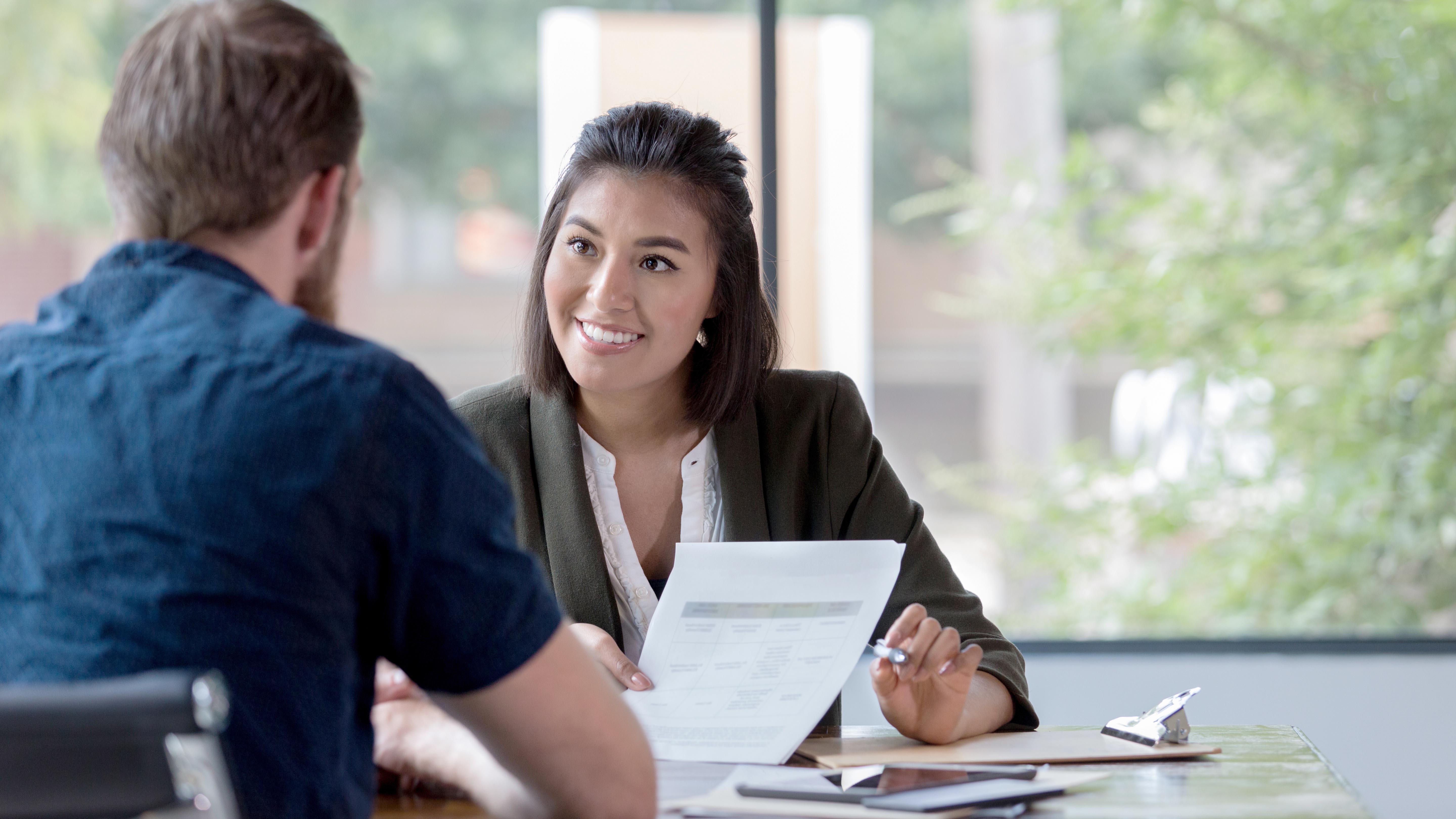 Female banker smiles while showing a document to a male customer